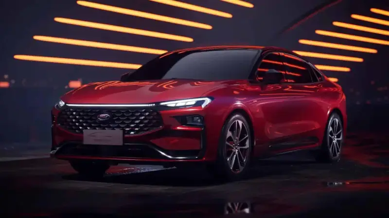 Czerwony Ford Mondeo MK6 z nowoczesnym designem, błyszczącym grillem i ostrymi światłami LED, prezentowany na tle pomarańczowych świateł.