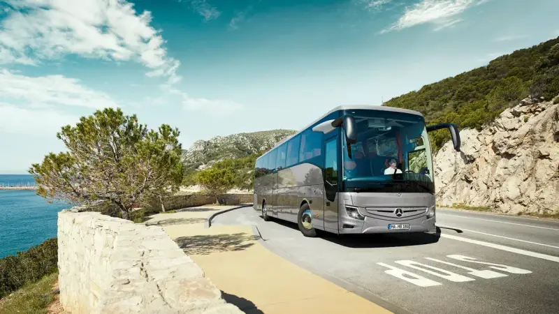 Srebrny Mercedes Tourismo jedzie malowniczą trasą nad morzem.