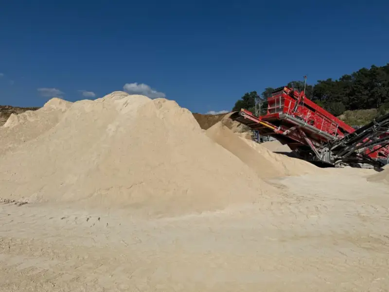 Góra piasku, prawdopodobnie wapno węglanowe, obok czerwonej maszyny do przesiewania na placu budowy.