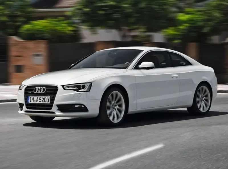 Białe Audi A5 Coupe pędzi po drodze, jego sylwetka jest dynamiczna i elegancka.