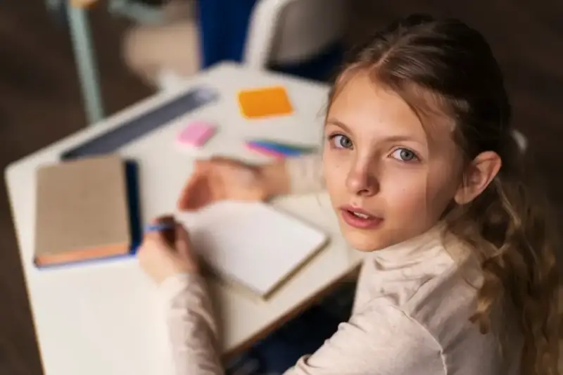 Dziewczynka zmagająca się z dysleksją rozwojową próbuje pisać w zeszycie, patrząc z nadzieją na pomoc.