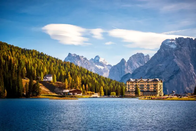 Lago alpino con hotel giallo e boschi autunnali, ideale tra i laghi da visitare in giornata.