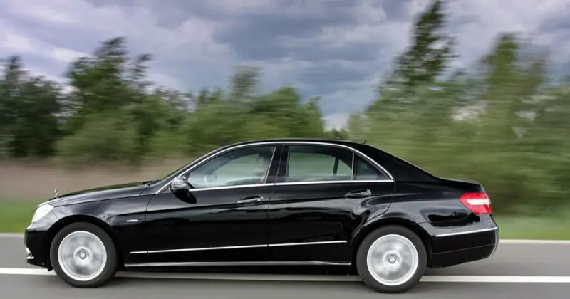Czarny Mercedes E350 pędzi po drodze, mijając rozmyte zielone drzewa.
