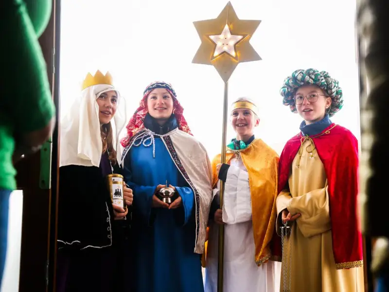 Vier Kinder als Sternsinger evangelisch verkleidet, mit Stern und Spendenbüchse, stehen vor einer Tür.