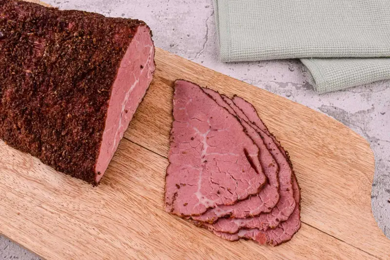 Kawałek pastrami, co to jest? Aromatyczne, peklowane i wędzone mięso wołowe, pokrojone w cienkie plastry, leży na desce.