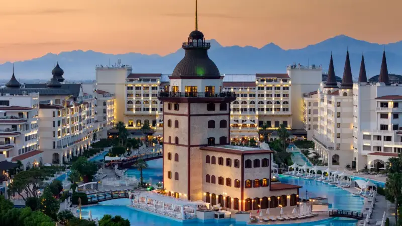 Luksusowy hotel z basenami i wieżą, idealny na wakacje all inclusive w Turcji. Góry w tle.