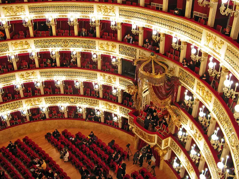 Elegancka loża w teatrze, z czerwonymi aksamitnymi siedzeniami i złotymi zdobieniami, czeka na widzów.