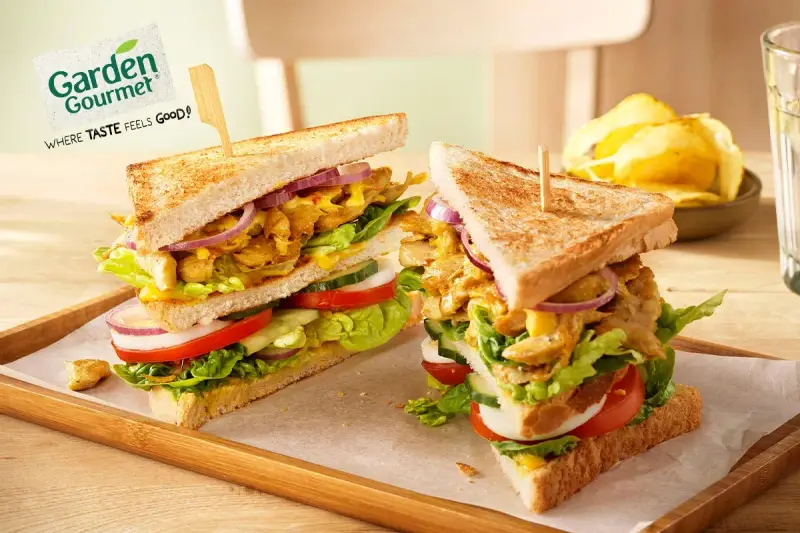 Zwei üppige Garden Gourmet Club Sandwiches mit knackigem Salat, Tomaten, Gurken und Zwiebeln auf getoastetem Brot.