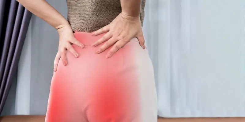 Kobieta trzyma się za bolące biodra i dolną część pleców, gdzie widoczne są czerwone plamy. To mogą być objawy korzonków.