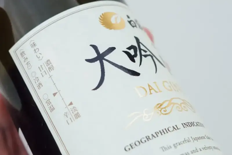 Butelka sake z napisem "DAI GIN". Na etykiecie widać skalę smaku i temperatury podania.