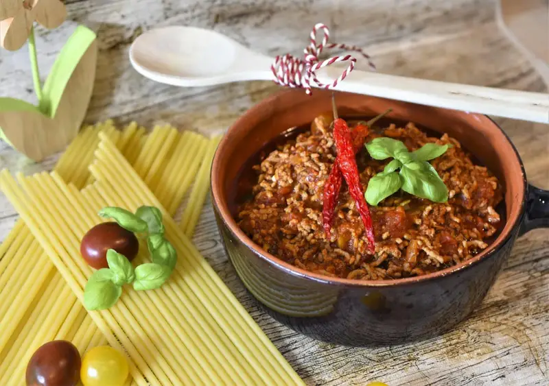 Un saporito sugo alla bolognese in una ciotola di terracotta, pronto per condire spaghetti, con pomodorini e basilico.