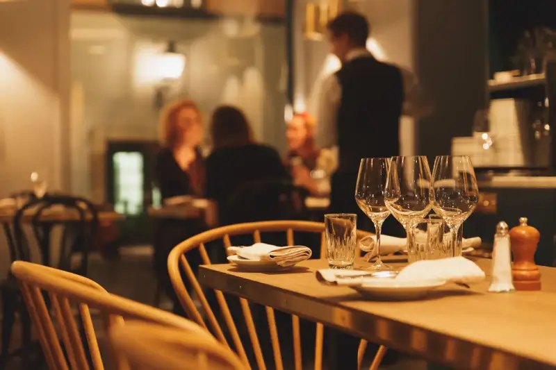 Ett dukat bord med vinglas och servetter, redo för en matvandring i Stockholm. I bakgrunden syns gäster och personal i en mysig restaurangmiljö.