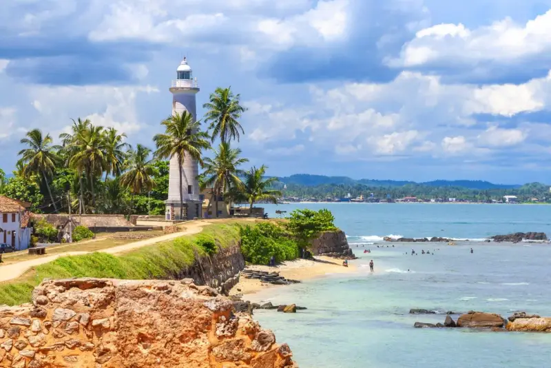 Latarnia morska na Sri Lance, otoczona palmami, z widokiem na ocean i plażę. Idealne miejsce na wakacje, warto sprawdzić wizę Sri Lanka.