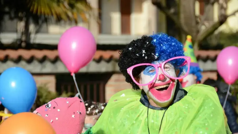 Uśmiechnięty animator w peruce i okularach, otoczony balonami, przygotowuje się do zabawy.