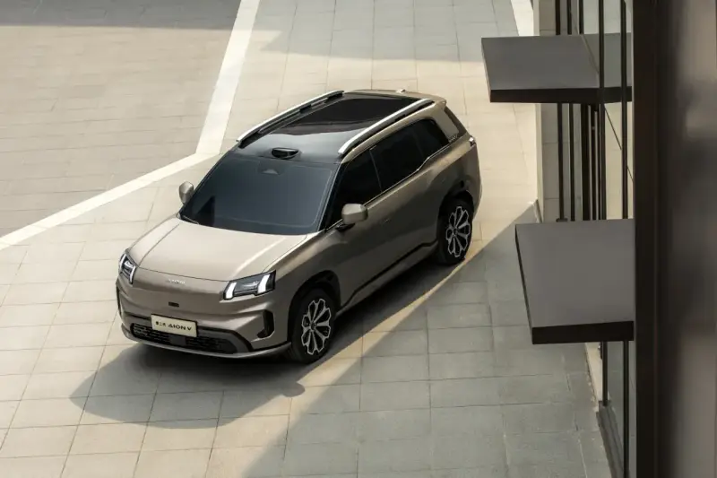 Szary elektryczny SUV GAC Aion V z czarnym dachem i relingami, zaparkowany na zewnątrz.