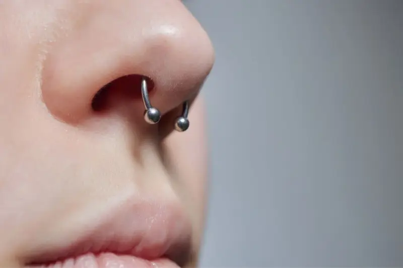 Zbliżenie na nos z kolczykiem typu septril piercing. Metalowy okrąg z dwoma kulkami subtelnie zdobi przegrodę nosową.