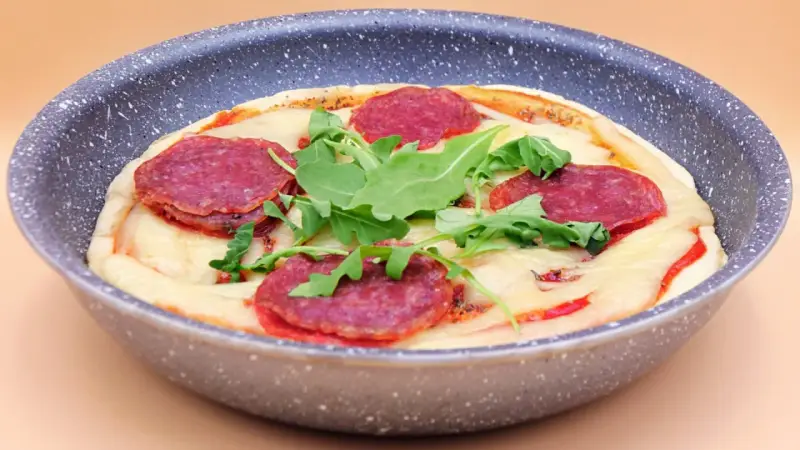 Mini pizza na patelni z serem, rukolą i plasterkami pikantnej salsiccii.