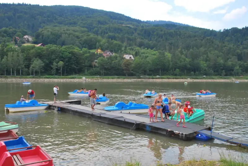 Wakacyjny dzień na Jeziorze Żywieckim. Ludzie pływają na rowerach wodnych, czując się jak na karaibskiej plaży.