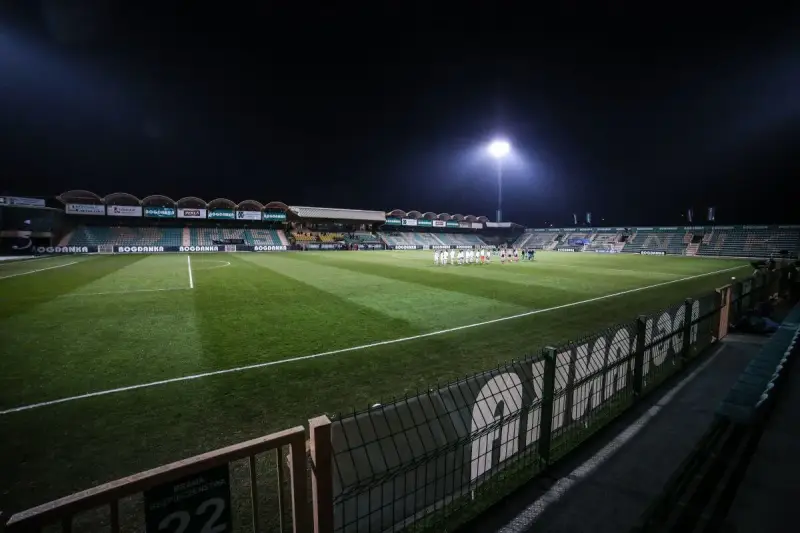 Piłkarze na murawie stadionu Górnik Łęczna, oświetlonego jupiterami.