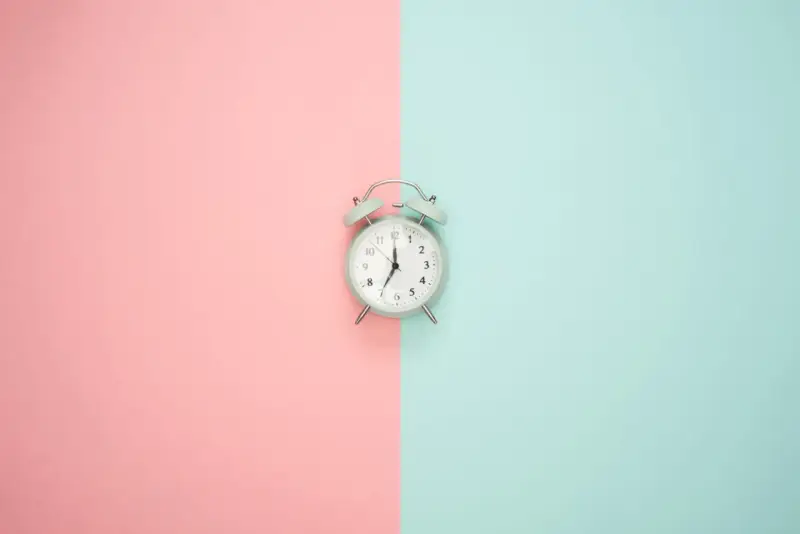 Wecker auf rosa und blauem Hintergrund. Zeit für Stundenreduzierung Schwangerschaft Gehalt.