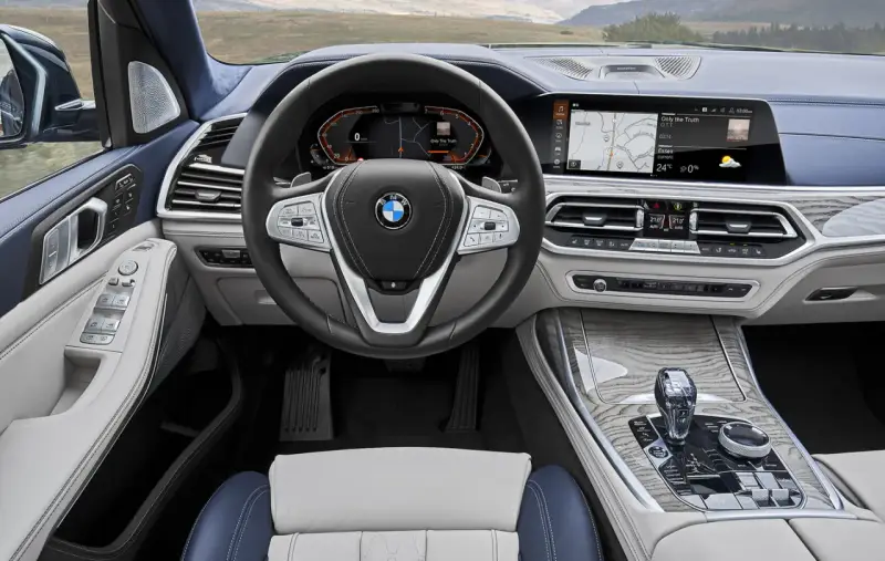 Wnętrze BMW X7: kierownica, ekran multimedialny z nawigacją i muzyką, panel klimatyzacji, dźwignia zmiany biegów.
