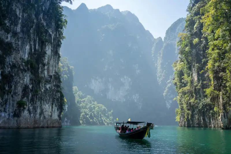 En båt färdas på turkost vatten genom dramatiska kalkstensklippor i Khao Sok nationalpark.