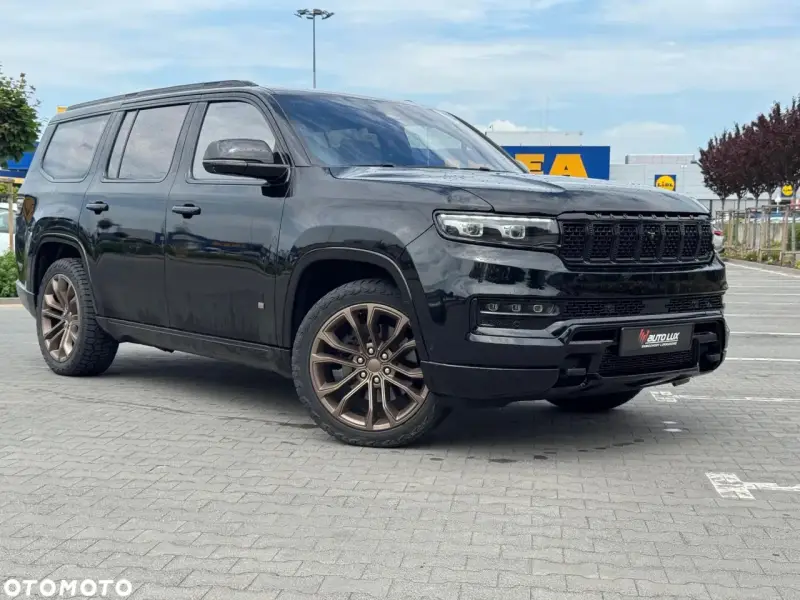 Czarny Grand Wagoneer z brązowymi felgami stoi na parkingu przed sklepami.