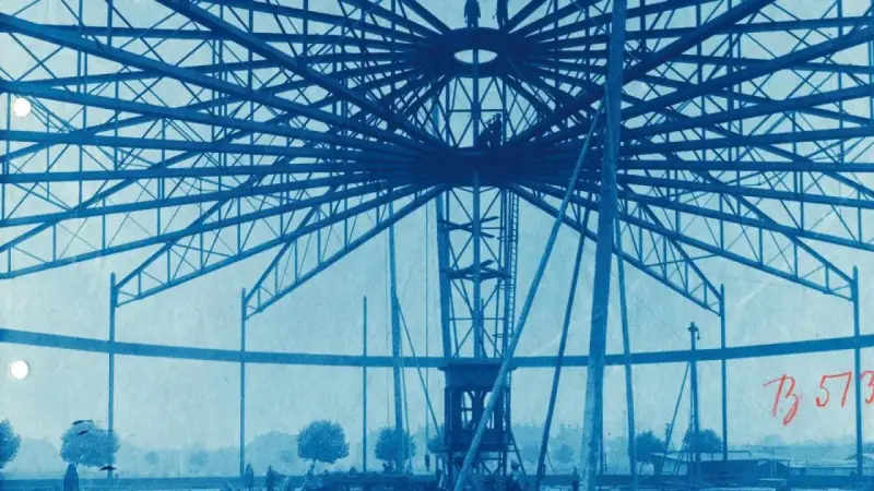 Bau des Riesenrades am GHH Oberhausen. Die Stahlkonstruktion ragt in den Himmel, Arbeiter sind auf der Spitze zu sehen.