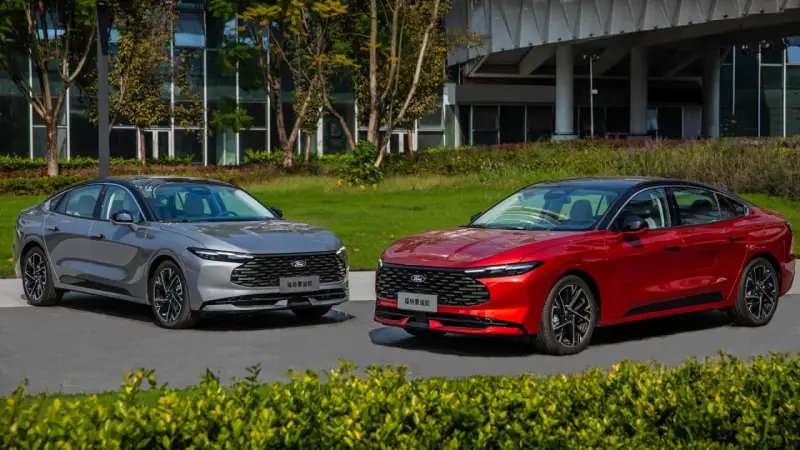 Dwa nowe Fordy Mondeo mk6, jeden czerwony, drugi szary, stoją obok siebie na tle nowoczesnego budynku i zieleni.