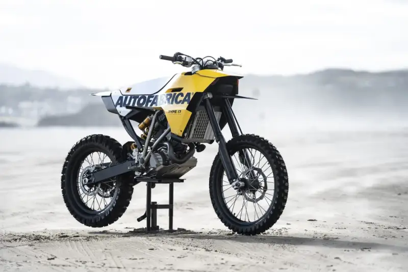 Żółto-biały motocykl customowy Autofabrica Type 17, bazujący na BMW G450X, stoi na plaży.