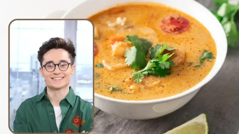 Uśmiechnięty mężczyzna w okularach prezentuje aromatyczną zupę tajską z krewetkami i pomidorkami, ozdobioną świeżą kolendrą.