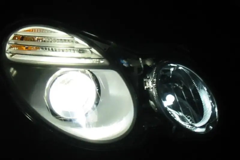 Jasny ksenon rozświetla reflektor, ukazując jego nowoczesny design i pomarańczowe kierunkowskazy.