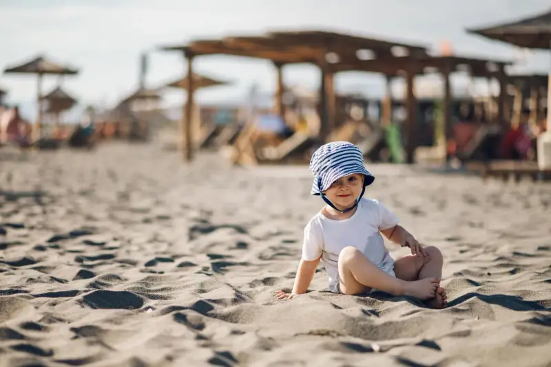 Uroczy maluch w pasiastym kapelusiku na plaży. Idealne miejsce, gdzie na wakacje z rocznym dzieckiem, by cieszyć się słońcem i piaskiem.