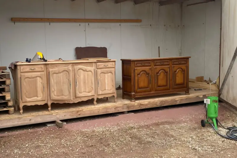 Deux commodes en bois, l'une brute et l'autre vernie, témoignent d'une **réparation meuble en bois**. Un équipement de sablage est prêt à l'emploi.