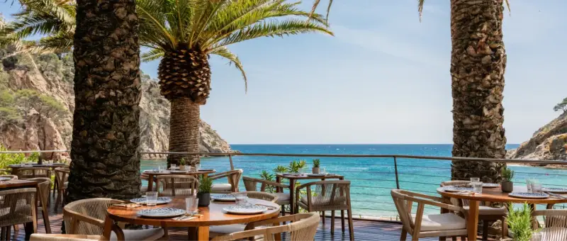 Mesas de restaurante con vistas al mar en el pola giverola resort, bajo palmeras.