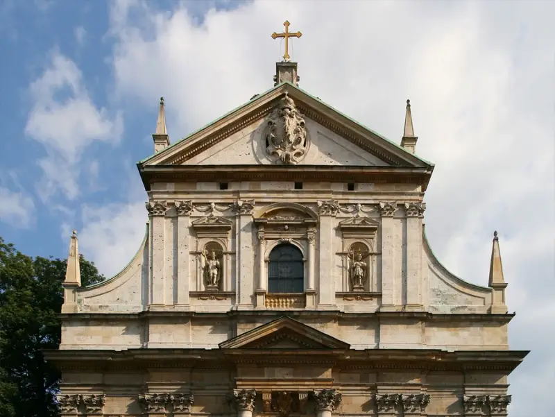 Bogata fasada kościoła w stylu barokowym, z rzeźbami i zdobieniami, pod błękitnym niebem.