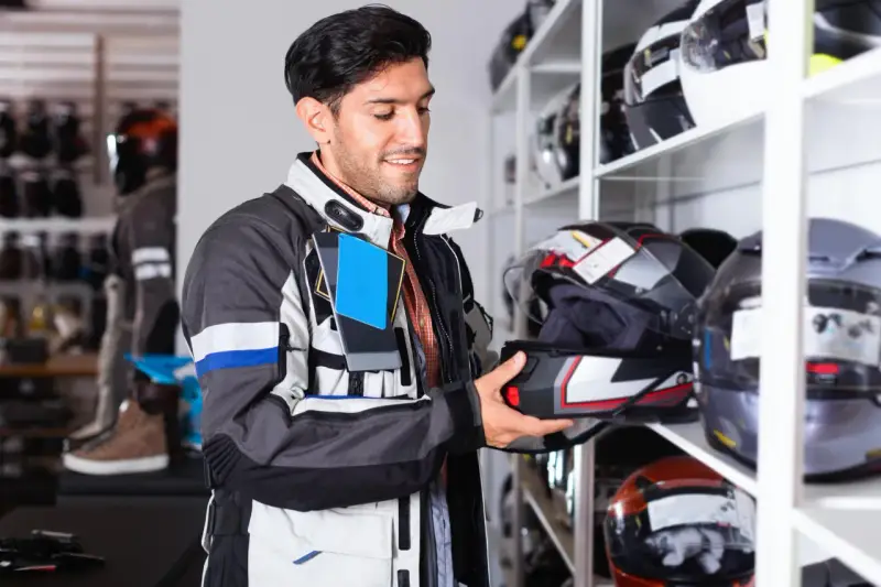 Uomo in negozio di moto esamina un casco, cercando la taglia XS. Corrisponde a una misura piccola, ideale per teste più minute.