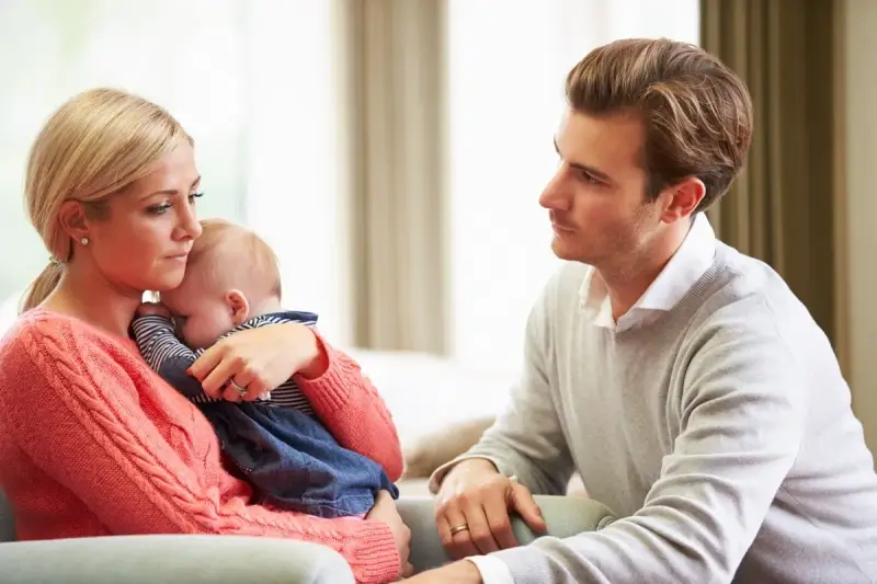 Zmartwiona mama tuli dziecko, a ojciec patrzy z troską. Czy to baby blues? Co to za uczucie?