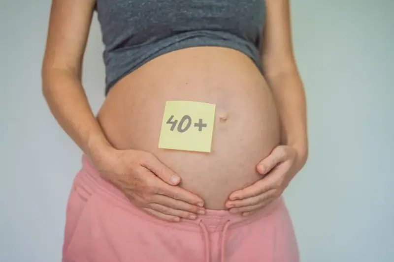 Brzuch kobiety w ciąży z karteczką "40+". To dowód, że ciąża po 40. jest możliwa i piękna.