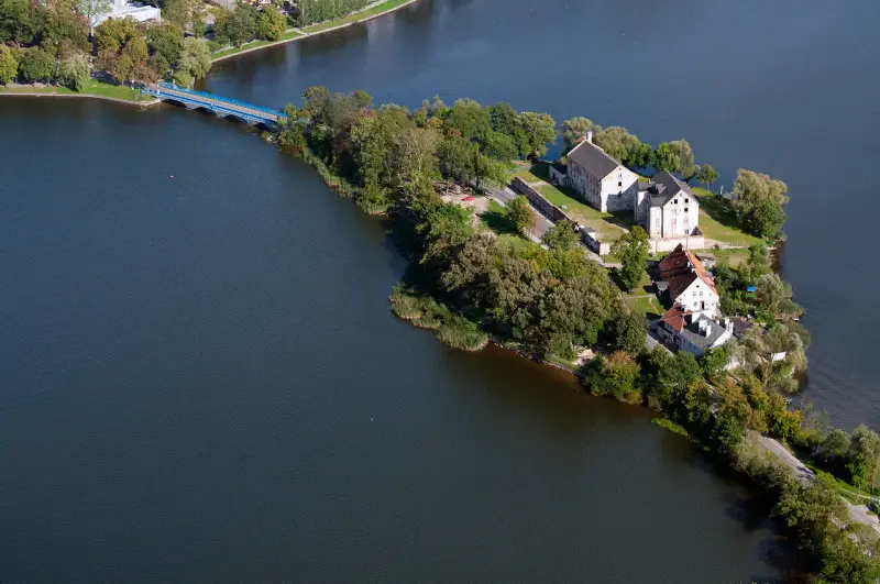 Ełk: zamek krzyżacki na wyspie, idealne miejsce na zwiedzanie. Most prowadzi do historycznych budynków otoczonych zielenią i wodą.