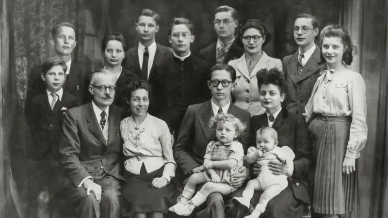 Gros plan sur une famille nombreuse posant pour une photo. On peut y voir des enfants, des adultes et des bébés. Une recherche sur Geneanet pourrait révéler leur nom de famille.
