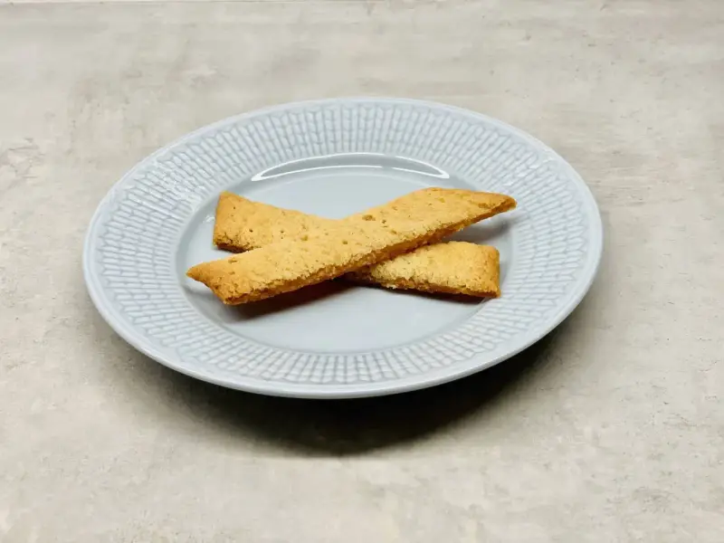 Två gyllene kolasnittar ligger korslagda på en ljusblå tallrik. Perfekt för ett enkelt kolasnittar recept.