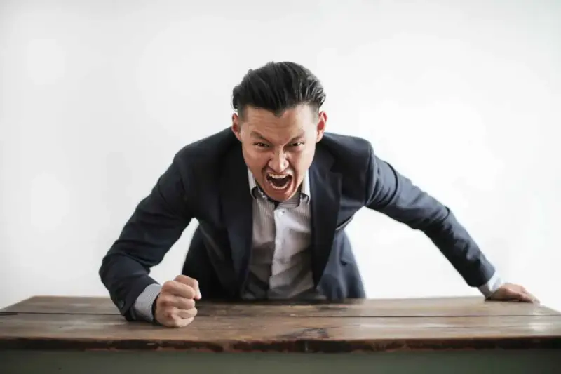 Wütender Mann im Anzug schreit über einen Tisch. Darf ein Lehrer Schüler anschreien?