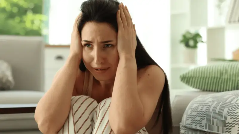 Kobieta z rękami na głowie, wyraźnie cierpiąca, jakby przeżywała epizod psychotyczny.