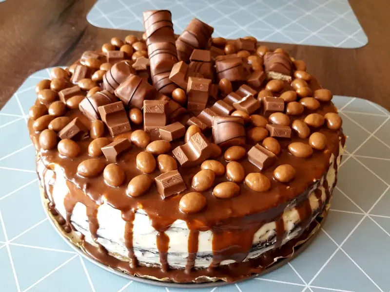 Pyszny tort kinder bueno, obficie udekorowany kawałkami batoników i czekoladowymi drażetkami, spływający karmelem.