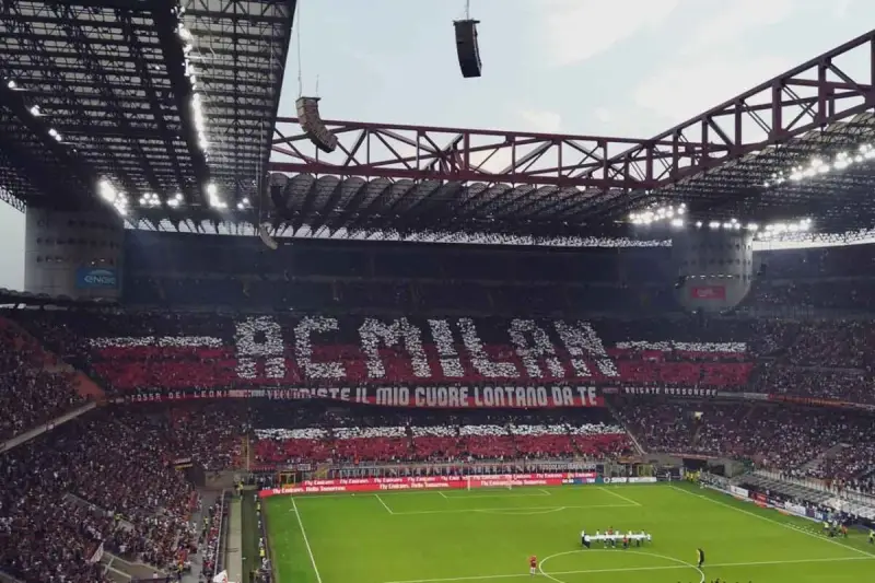 Trybuna stadionu San Siro w Mediolanie wypełniona kibicami AC Milan, tworzącymi napis "AC MILAN" i transparent "FOSSI DEI LEONI, VECCHIESTE IL MIO CUORE LONTANO DA TE".