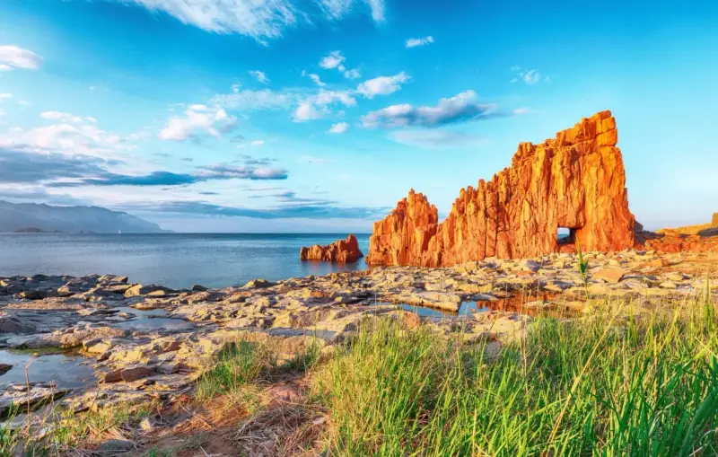 Scogliere rosse a picco sul mare blu, con un arco naturale, vicino ad Arbatax centro storico.