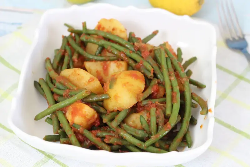 Fagiolini in umido con patate, un piatto saporito e colorato, servito in una ciotola bianca su una tovaglia a quadri.