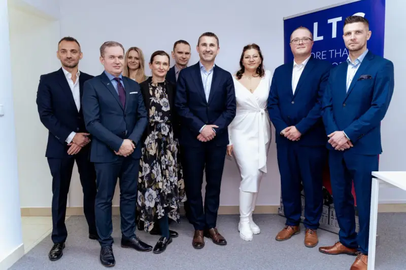 Grupa osób w garniturach i sukience pozuje do zdjęcia na tle banera.