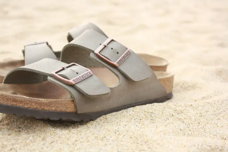 Sandali Birkenstock grigi sulla sabbia. Scopri come si lavano le Birkenstock per mantenerle perfette.